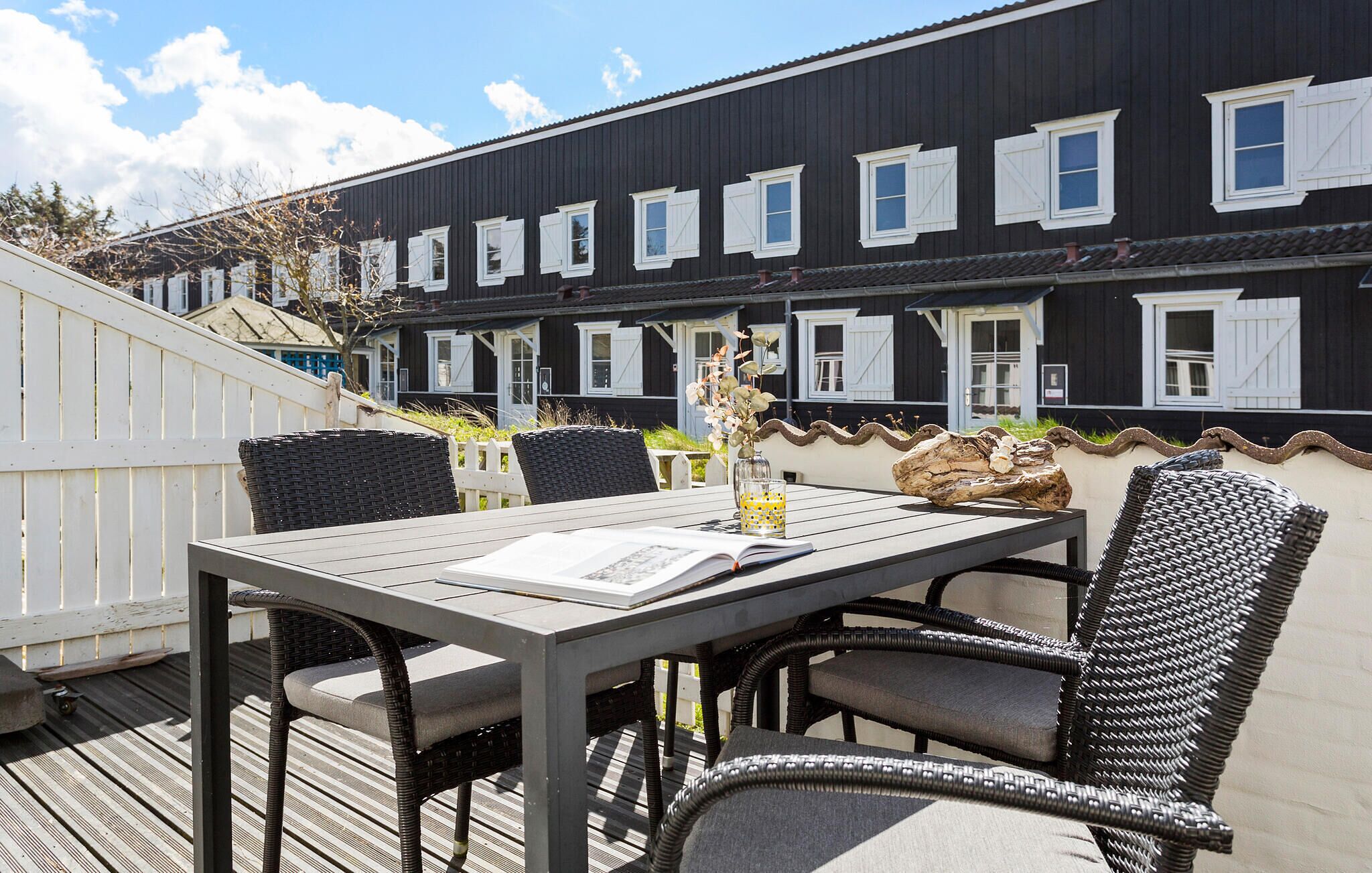 En terrasse med et bord, stole, en bog og et glas vand.