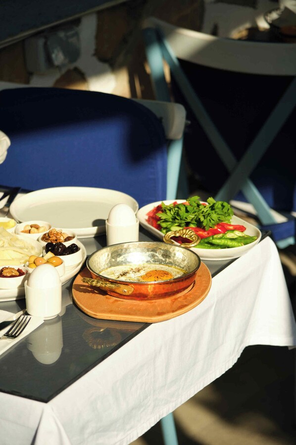 A table set with various dishes, including a bowl of soup, a plate of vegetables, and a plate of meat, all on a white tablecloth. - Cunda Pusula by Megaron Homes (Ayvalik)