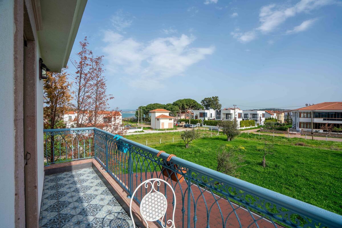 A balcony with a patterned floor, a metal railing, and a view of a green park and buildings in the distance.