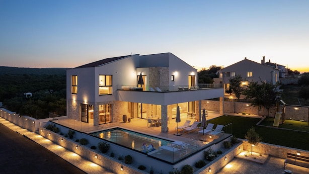 Ein modernes, zweistöckiges Haus mit Swimmingpool, Sitzgelegenheiten im Freien und Blick auf die umliegende Landschaft.