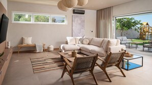 Ein modernes Wohnzimmer mit einem beigefarbenen Sofa, einem Holztisch, Korbstühlen und einem großen Fenster mit Blick ins Freie.