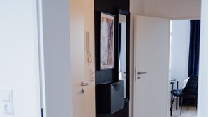 En hall med trägolv, vita väggar och en svart dörr med en inramad tavla.