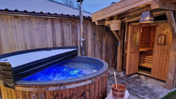 Un sauna en bois doté d’un bain à remous à ciel ouvert, d’un seau en bois et d’une porte de sauna.