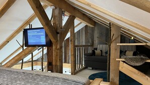 Une chambre à coucher aménagée en mezzanine, avec un plafond en bois, un lit, un canapé et un téléviseur fixé au plafond.