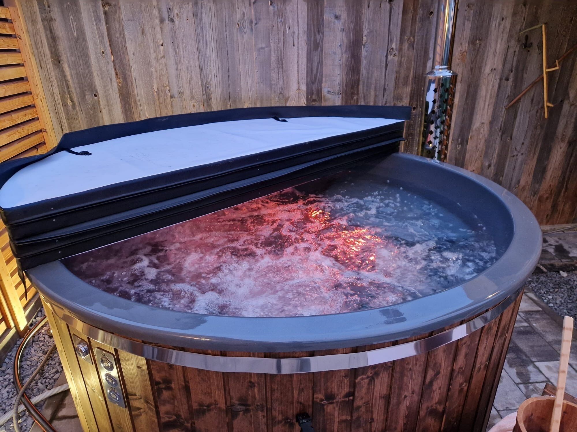 Un bain à remous avec une structure extérieure en bois et un couvercle en métal, entouré d’une clôture en bois.