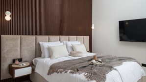 Une chambre moderne avec un grand lit, un mur recouvert de lambris en bois, un téléviseur fixé au mur et une table de chevet avec une lampe.