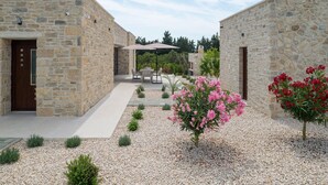 Un bâtiment en pierre doté d’un patio, d’un espace extérieur aménagé pour s’asseoir et d’un petit jardin avec des fleurs roses.