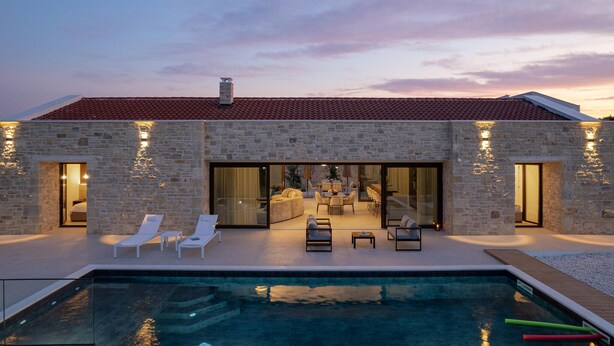 Un bâtiment en pierre doté d’une piscine, d’un espace extérieur aménagé et offrant une vue sur le coucher de soleil.
