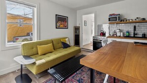A modern kitchen with a wooden table, a green sofa, and a window with a view of a building. - Queens Suite 1BR Free Parking (St. John's)