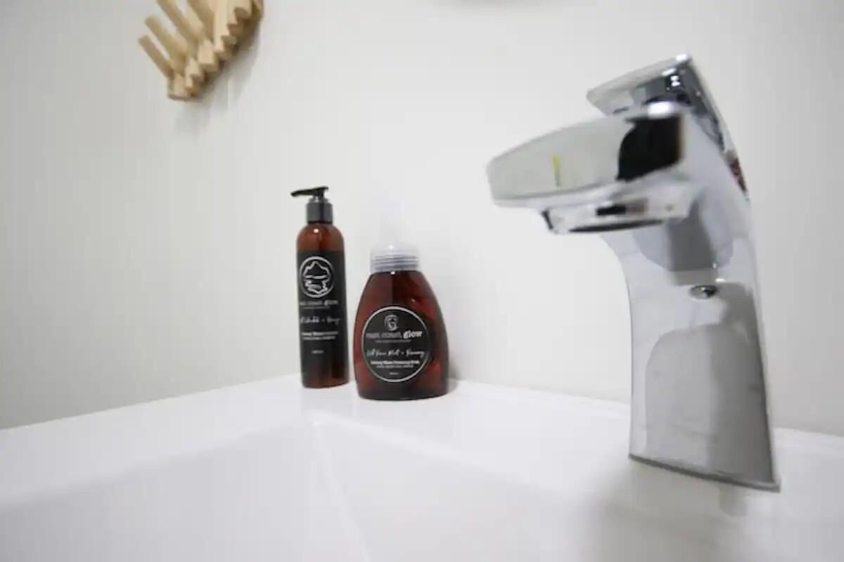 Une salle de bain avec un lavabo blanc, un robinet chromé et deux flacons de produits pour les soins capillaires.