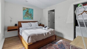 A bedroom with a wooden bed, a map on the wall, a wardrobe, and a small table. - Queens Suite 1BR Free Parking (St. John's)