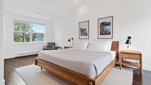 A modern bedroom with a wooden bed, a large window, and two framed pictures on the wall. - Wood House King Bd 2 Queens Fire Pit (St. John's)