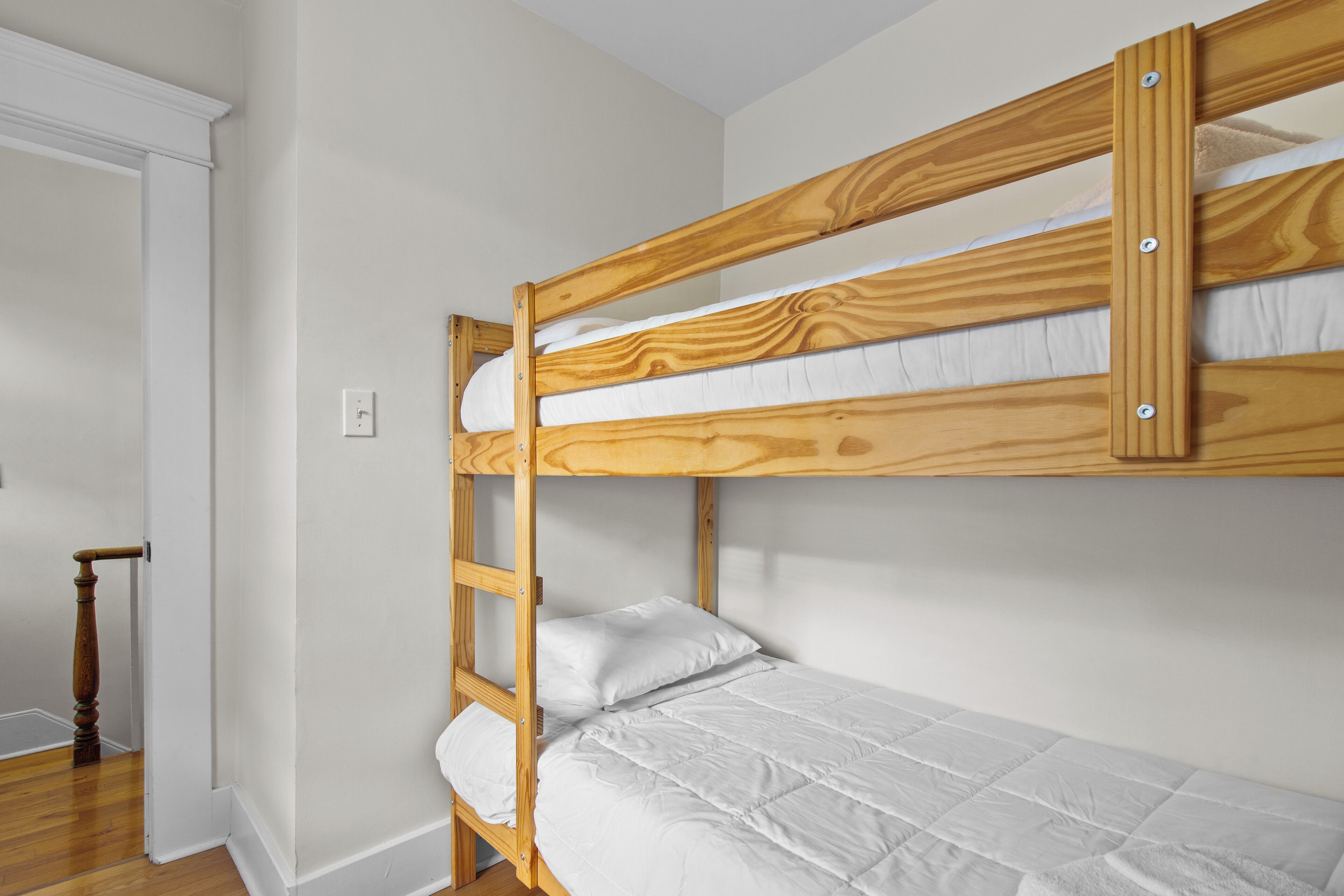 Een stapelbed met witte beddengoed in een kamer met witte wanden en houten vloer.