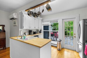 A kitchen with white cabinets, a wooden countertop, a stainless steel refrigerator, and a window with a view of greenery.