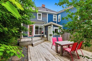 A wooden deck with a table and chairs, a house with blue siding and a red door, and a wooden fence.