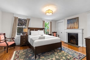 A hotel room with a large bed, a fireplace, a desk with a lamp, and a window with curtains.