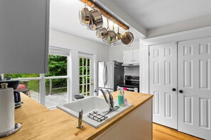 A modern kitchen with a wooden countertop, stainless steel appliances, and a hanging pot rack.