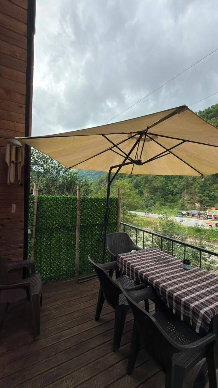 Un patio exterior con una mesa y sillas, una sombrilla grande y vistas a un paisaje verde.