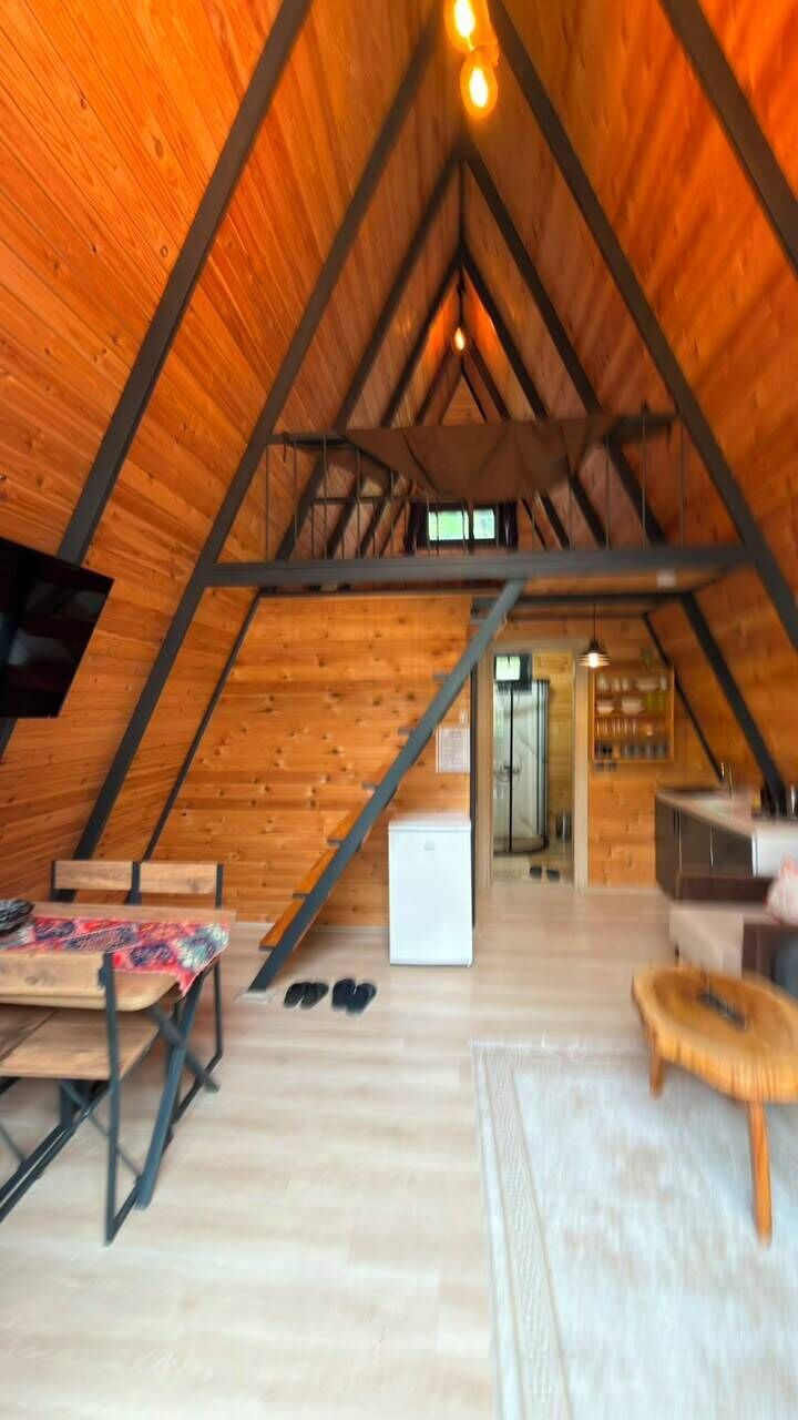 An attic room with a wooden ceiling, a bed, a desk, and a kitchen area.