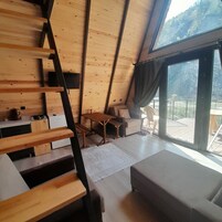 A modern loft bedroom with a wooden staircase, a sofa, a table, and a large window offering a view of the outdoors.