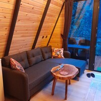 A cozy room with a dark brown sofa, two patterned pillows, a small wooden table with a knife and a decorative plate, and a glass door leading outside.