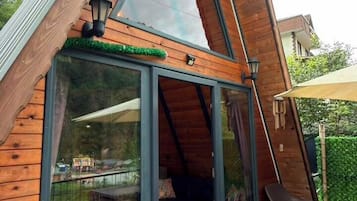 Una cabaña moderna de madera con techo inclinado, grandes puertas de vidrio y una terraza con mobiliario exterior.