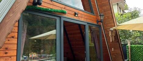 A modern wooden cabin with a sloped roof, large glass doors, and a deck with outdoor furniture.