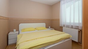 Un dormitorio con cama, mesitas de noche, un radiador y una ventana con cortinas translúcidas.