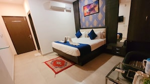 A hotel room with a bed, a red patterned rug, a television, and a wardrobe. - Hotel The Orchid (Agra)