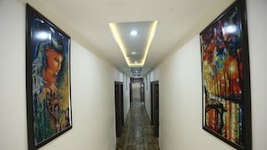 A hallway with two large framed paintings on either side, a wooden floor, and a ceiling with recessed lighting. - Hotel The Orchid (Agra)