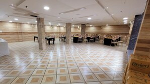 A spacious hall with a tiled floor, multiple tables with chairs, and a stage area. - Hotel The Orchid (Agra)