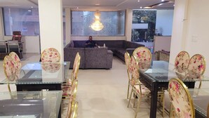 A modern living room with a glass dining table, floral chairs, a sofa, and a chandelier. - Hotel The Orchid (Agra)