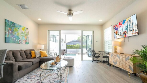 A modern living room with a grey sofa, glass coffee table, and a colorful rug. - Comfortable home Near Disney & Private Pool 17414 (Clermont)