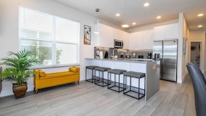 A modern kitchen with a central island, bar stools, and a yellow sofa. - Comfortable home Near Disney & Private Pool 17414 (Clermont)