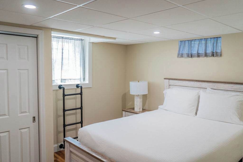 A hotel room with a bed, a nightstand with a lamp, a window with curtains, and a door.