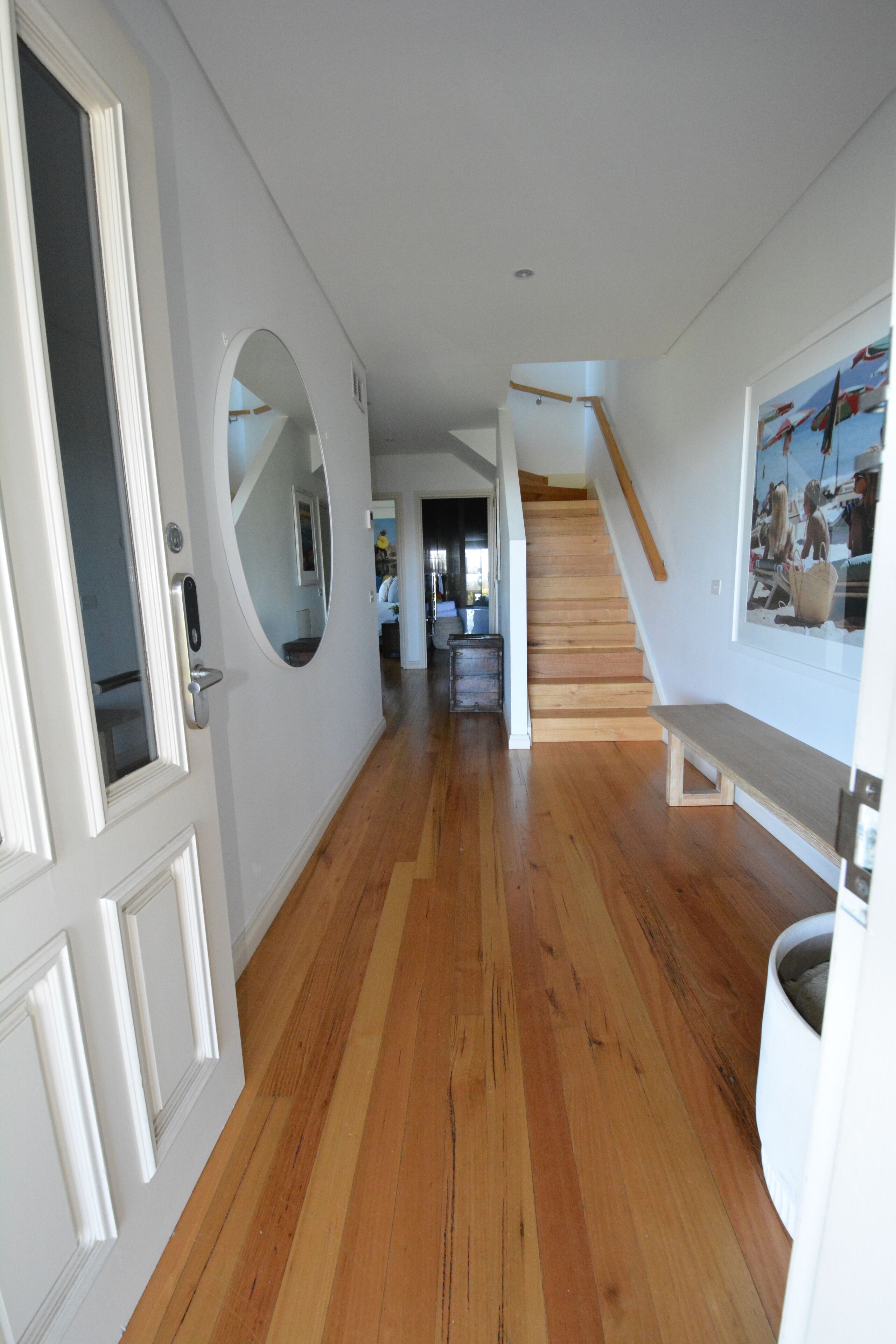 A hallway with wooden flooring, white walls, a staircase, and a bench.