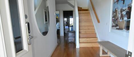 A hallway with wooden flooring, white walls, a staircase, and a bench.