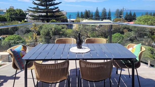 A wooden deck with a table and wicker chairs, overlooking a coastal landscape with trees and a view of the sea. - Bayview Apartment Sorrento, a family-friendly haven 350 meters from the beach.   (Sorrento)