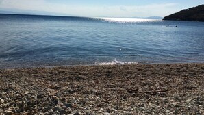 Ein kiesiger Strand mit ruhigem Wasser und fernen Bergen.