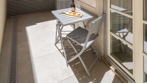 Un pequeño patio exterior con una mesa, sillas, un portón corredero y una ventana con persianas.