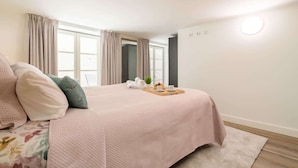 Un dormitorio con una cama, una mesita de noche con una bandeja de desayuno y una ventana con cortinas.