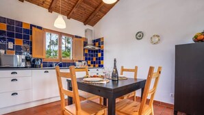 A kitchen with a tiled backsplash, wooden chairs, a black table, and a window.