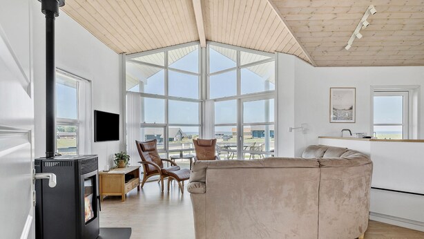 A modern living room with a large window, a fireplace, a sofa, and a kitchen area.