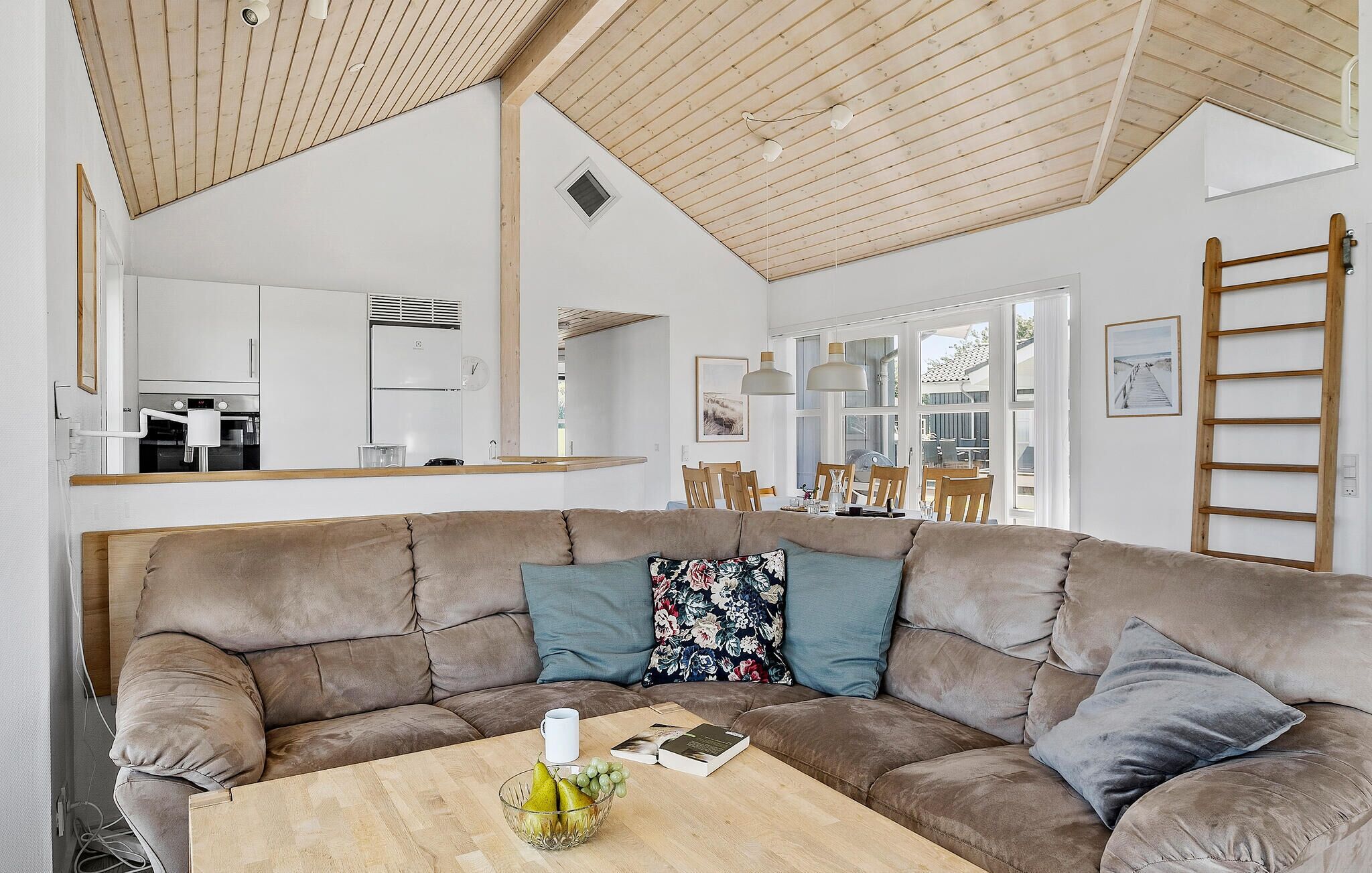Ein modernes Wohnzimmer mit einem großen braunen Ecksofa, einem Holztisch und einer Küche im Hintergrund.