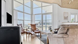 A spacious living room with a large window, a fireplace, leather chairs, and a sofa.