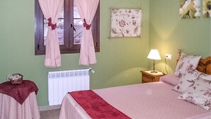 Ein Schlafzimmer mit Bett, Nachttisch, Lampe, einem Fenster mit Vorhängen, einer Heizung und einer Wanddekoration.