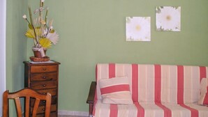 Ein Zimmer mit einem Holzsessel, einer Holzkommode, einem gestreiften Sofa und einer Wand mit zwei gerahmten Bildern.