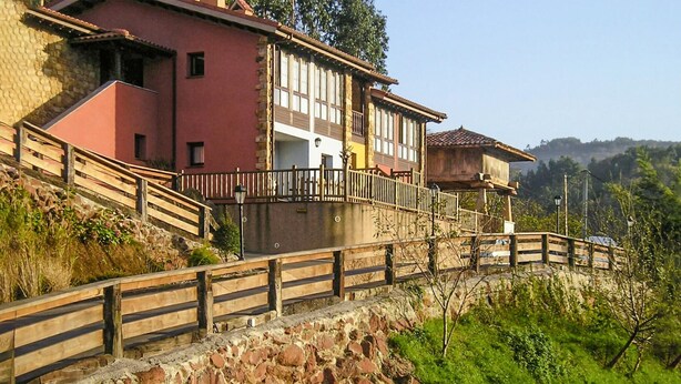 Eine steinerne Stützmauer mit einer hölzernen Treppe, die zu einem Gebäude mit roter Fassade und einem Balkon führt.
