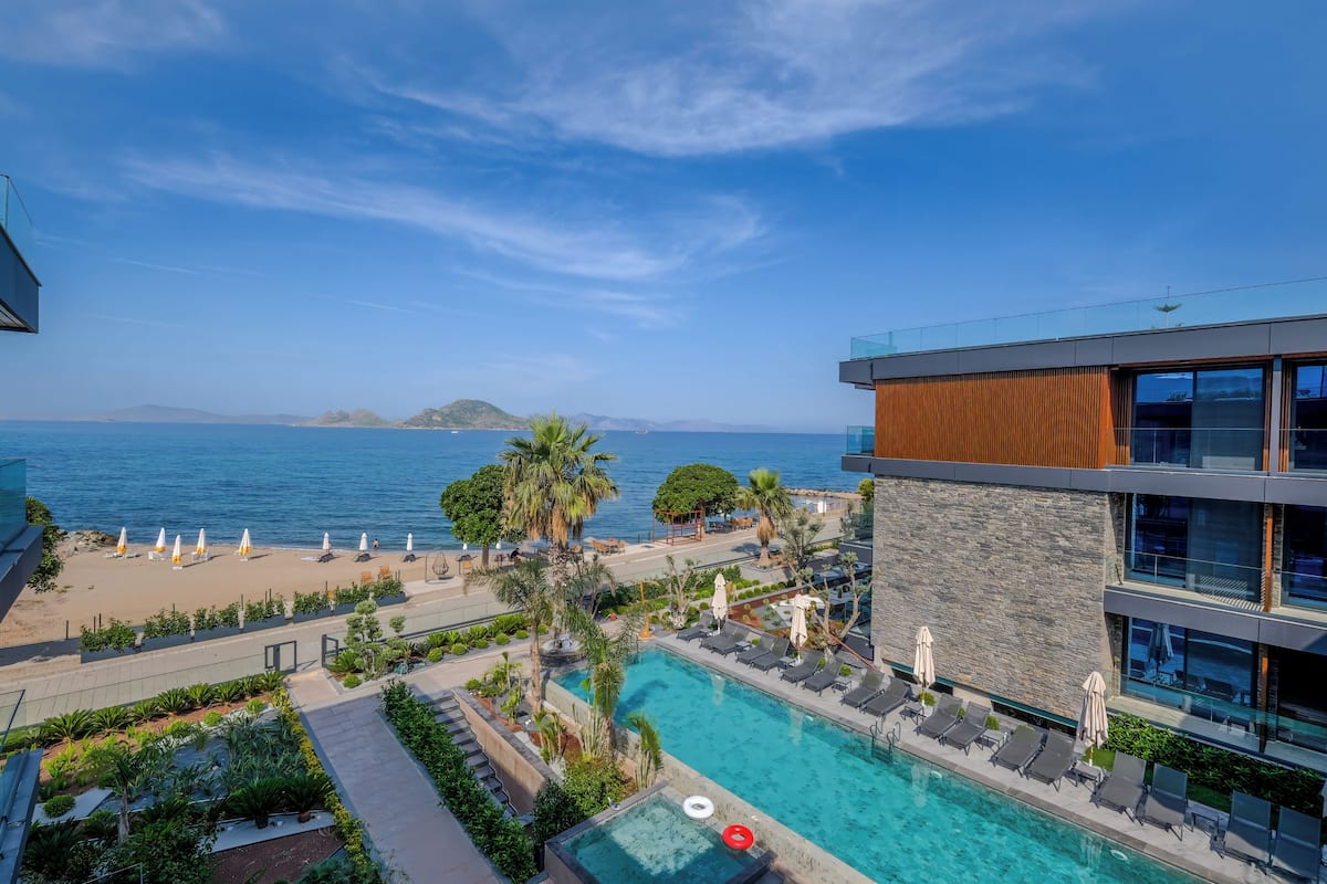 A modern hotel with a pool, beach view, and palm trees.
