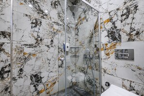 Ein modernes Badezimmer mit einer gläsernen Duschkabine, Marmorwänden und einem weißen Waschbecken.